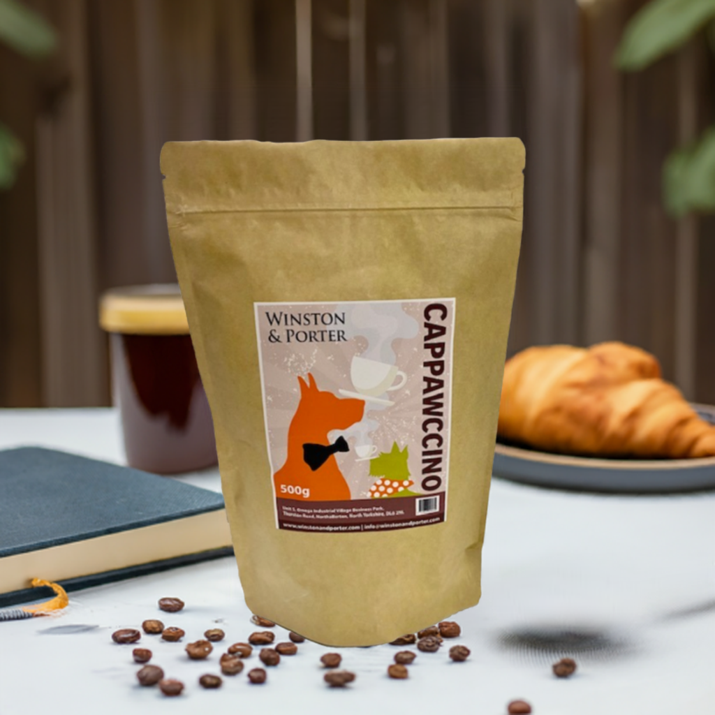 A pouch of Cappawccino dog-friendly coffee alternative by Winston & Porter, displayed on a table with coffee beans scattered in front and a croissant to the side.